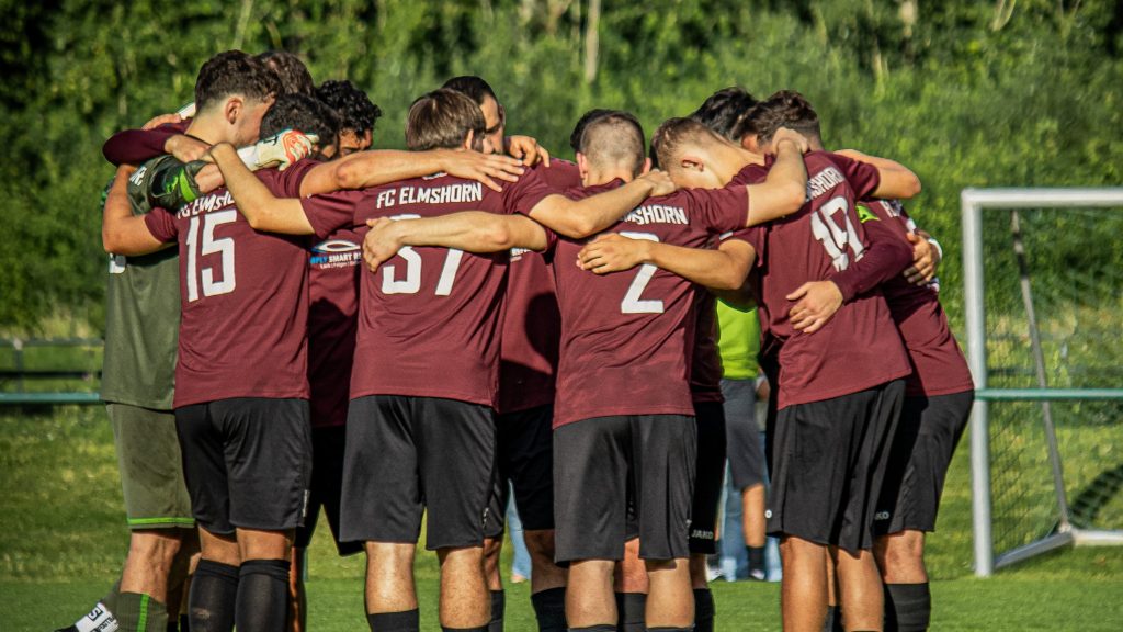 Spieler der Herrrenmannschaft des FC Elmshorn stehen in einer Traube auf einem Fussballplatz.