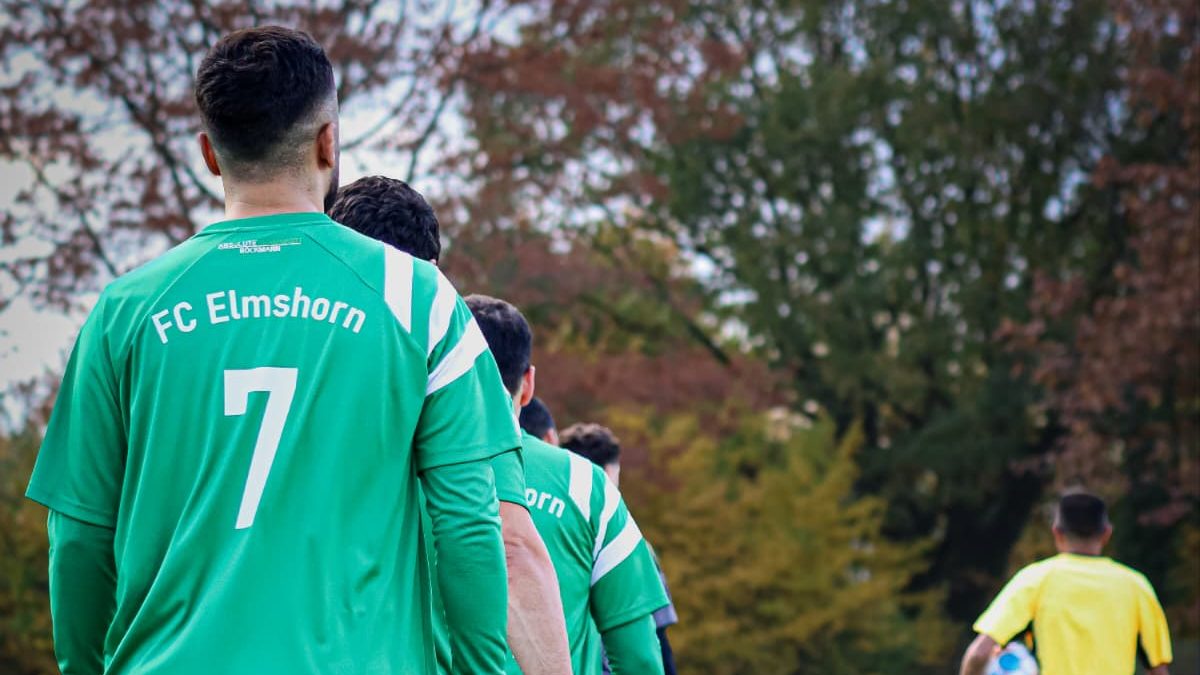 Spieler vom FC Elmshorn gehen über das Feld. Ein Schiri ist im Hintergrund zu sehen.